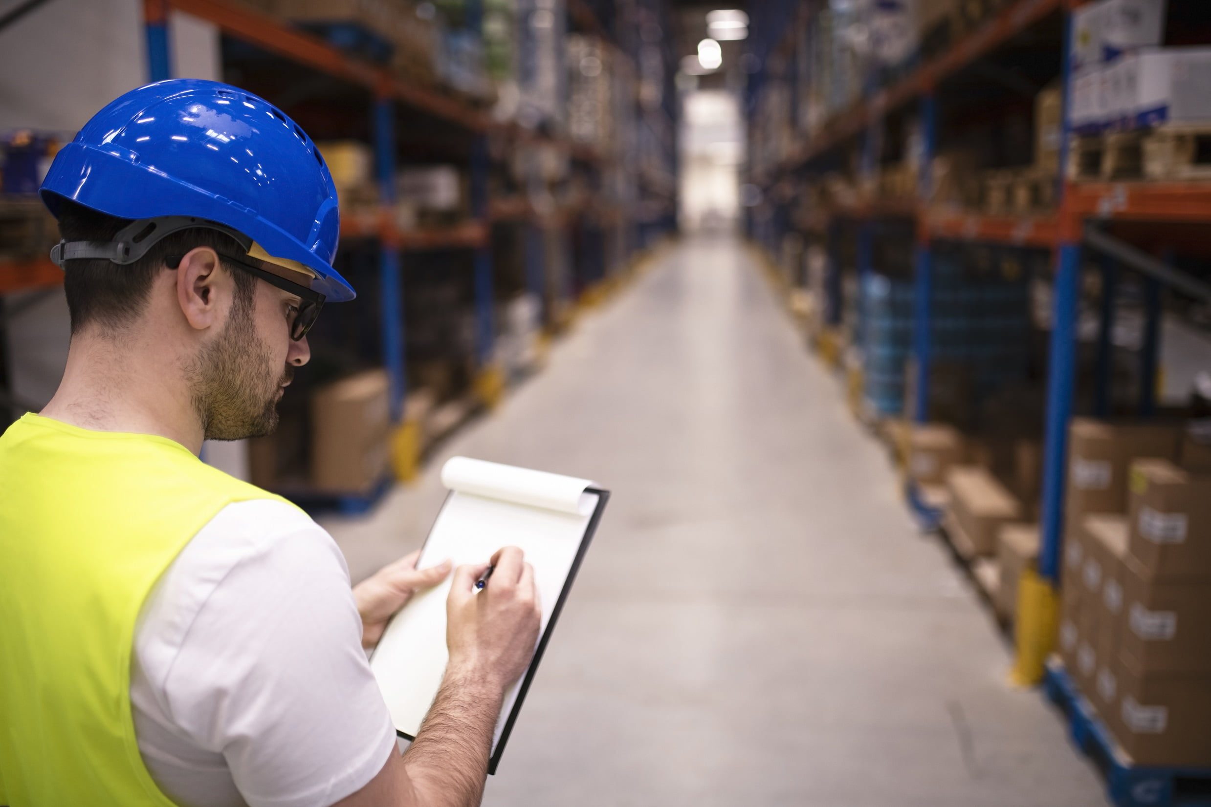 Factory worker holding clipboard and checking inventory of warehouse storage department.